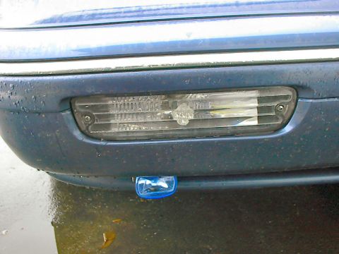 1985 Mercury Grand Marquis - Close-up of a car's front bumper showing a fog light and an additional blue light.
