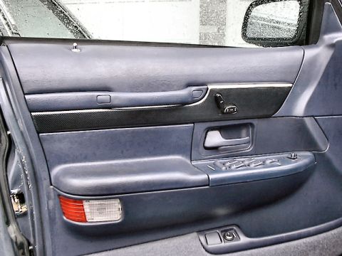 1985 Mercury Grand Marquis - Close-up of a car's interior door panel, showing the power window controls and a carbon fiber accent strip.