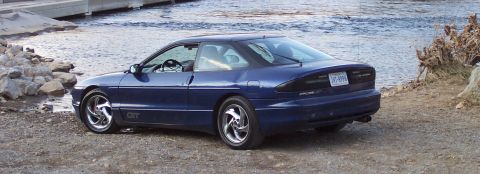 1994 Ford Probe - A blue 1994 Ford Probe GT is parked on a gravelly shore next to a body of water.