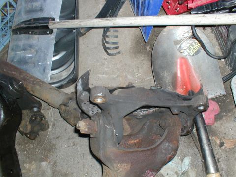 1979 Ford Bronco - Rusty vehicle spindle and brake caliper bracket assembly with other parts in background.
