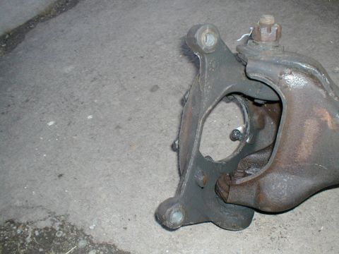 1979 Ford Bronco - A close-up view of an automotive suspension component, likely a spindle or knuckle, resting on a concrete surface. The SuperMotors logo is…