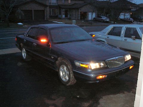 1985 Mercury Grand Marquis - A dark blue 1996 Mercury Grand Marquis sedan is parked in a driveway, showing its front grille and illuminated turn signals.