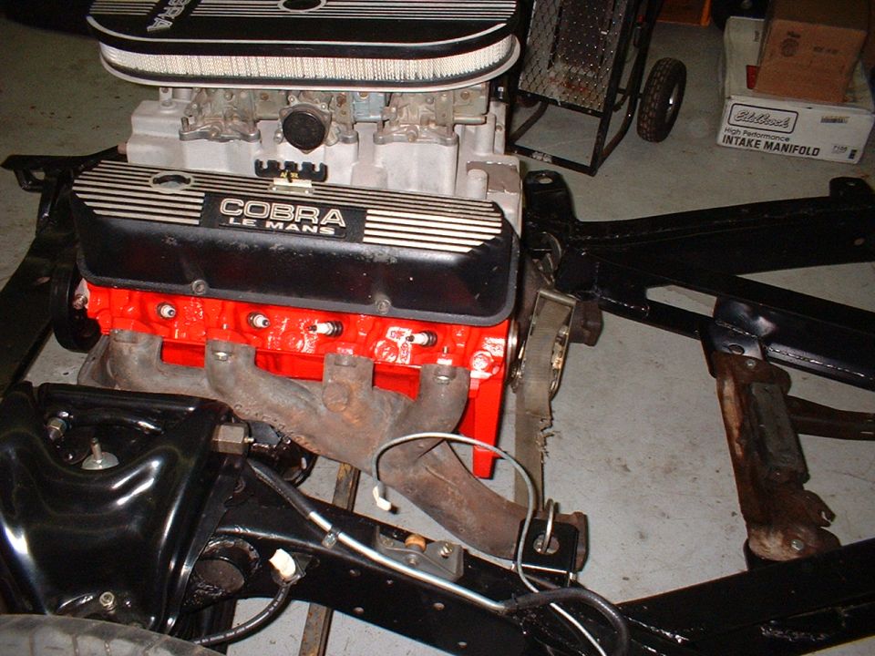 Red Ford V8 with Cobra Le Mans valve covers and dual carburetors mounted in a bare black chassis