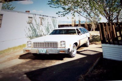 1972 Ford Ranchero - A white station wagon is parked in front of a white building with a wooden fence to the right.