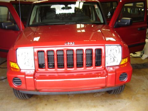 1997 Ford Taurus - The front grille and headlights of a red Jeep Commander are visible with its doors open.