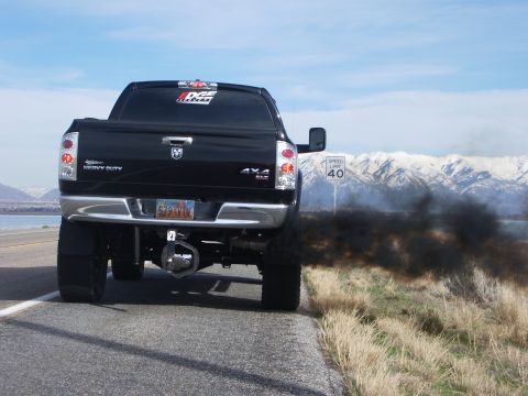2005 Dodge 2500 - A black Dodge 2500 pickup truck is seen from the rear, driving on a road and emitting a large cloud of black smoke.