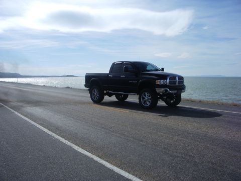 2005 Dodge 2500 - A black 2005 Dodge 2500 pickup truck is seen driving on a road beside a large body of water under a cloudy sky.