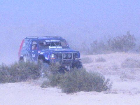 Blue off-road race SUV with red rear panel among desert brush in dust