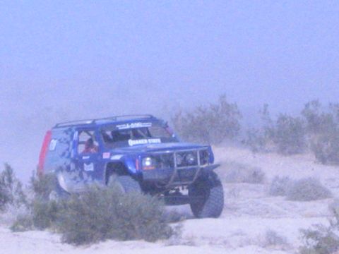 Blue Quaker State race SUV with roof rack on desert sand near brush