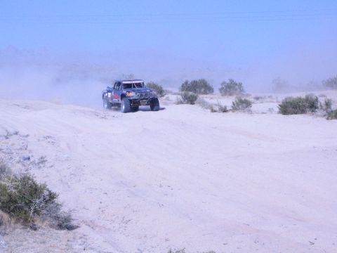 Dark off-road race truck on a desert sand rise with dust and brush