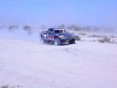 Dark blue race truck with number on desert sand throwing dust