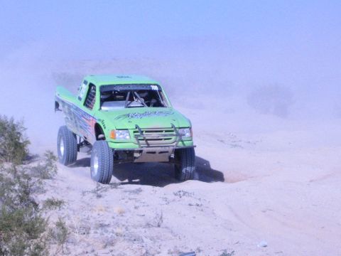 Bright green off-road race truck climbing a sandy desert berm