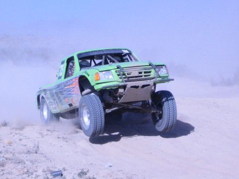 Green off-road race truck launching off a desert rise with front wheels in air