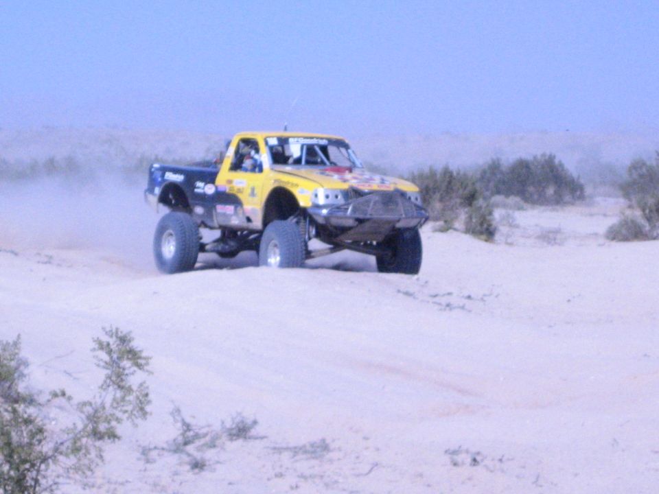 Yellow and blue off-road race truck jumping over a desert berm
