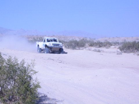 White off-road race truck driving down a wide sandy desert trail