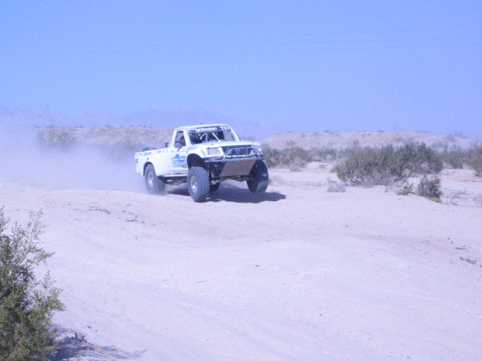 White off-road race truck racing along a sandy desert track
