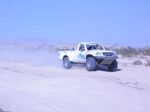 White race truck with blue graphics on a sandy desert course
