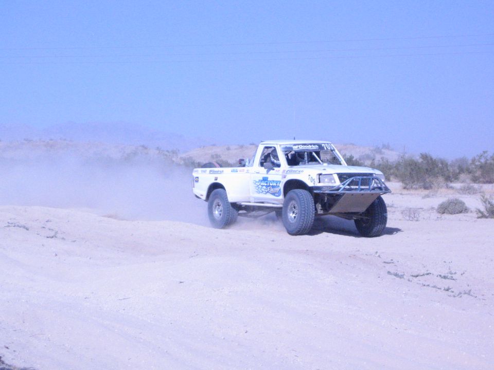 White race truck with blue graphics on a sandy desert course