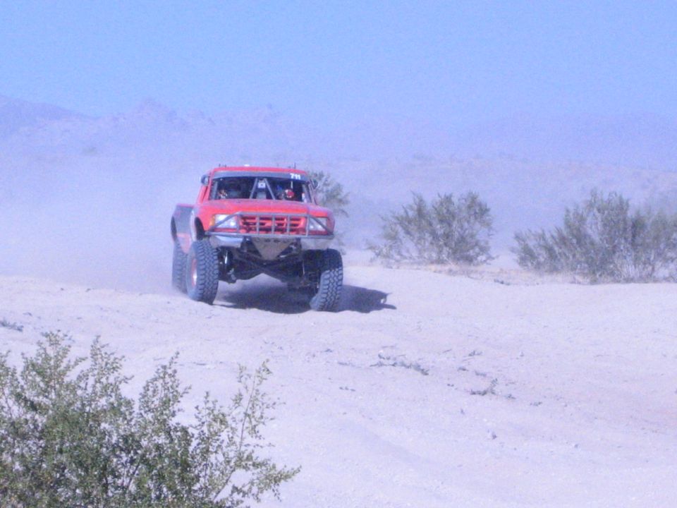 Red off-road race truck cresting a sandy berm in the desert