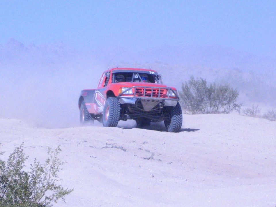 Red off-road race truck jumping over a sandy desert berm