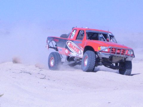 Red and black race truck with Maxxis graphics jumping in the desert