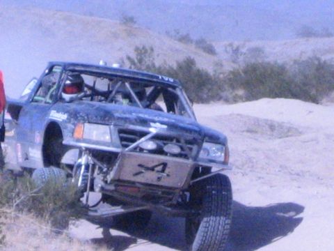 Blue off-road race truck with number 4 on front skid plate in desert