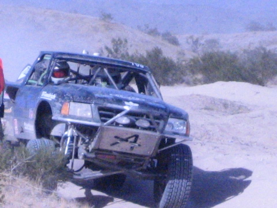 Blue off-road race truck with number 4 on front skid plate in desert