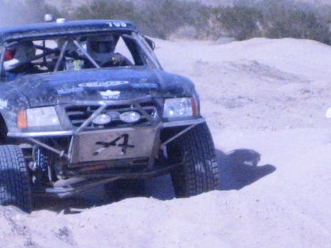 Blue off-road race truck with number 4 skid plate and roof lights in sand