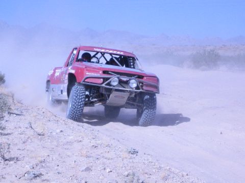 Dark red off-road race truck powering down a sandy desert trail