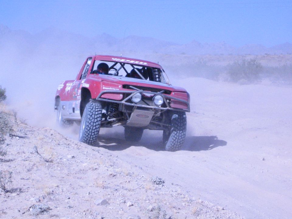 Dark red off-road race truck powering down a sandy desert trail