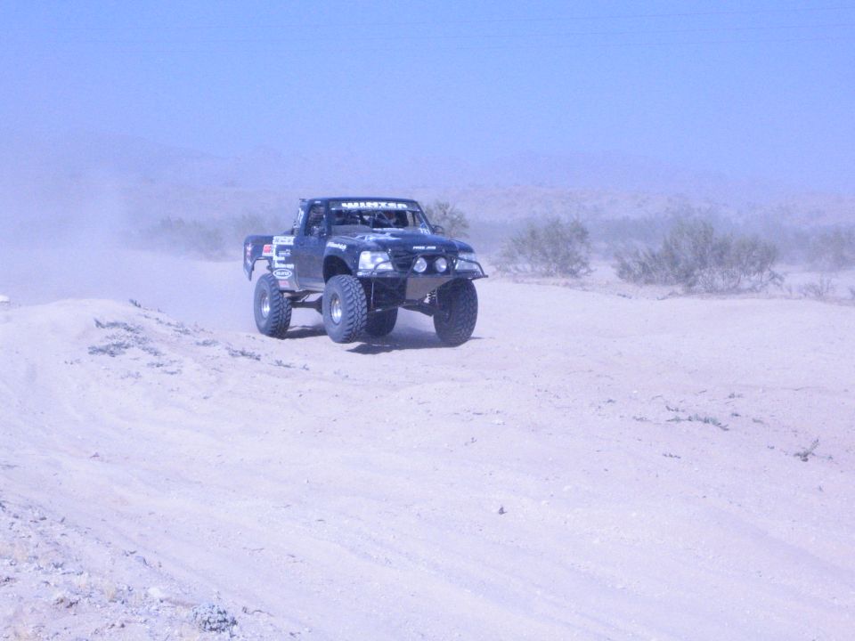 Dark off-road race truck cresting a sandy berm in open desert