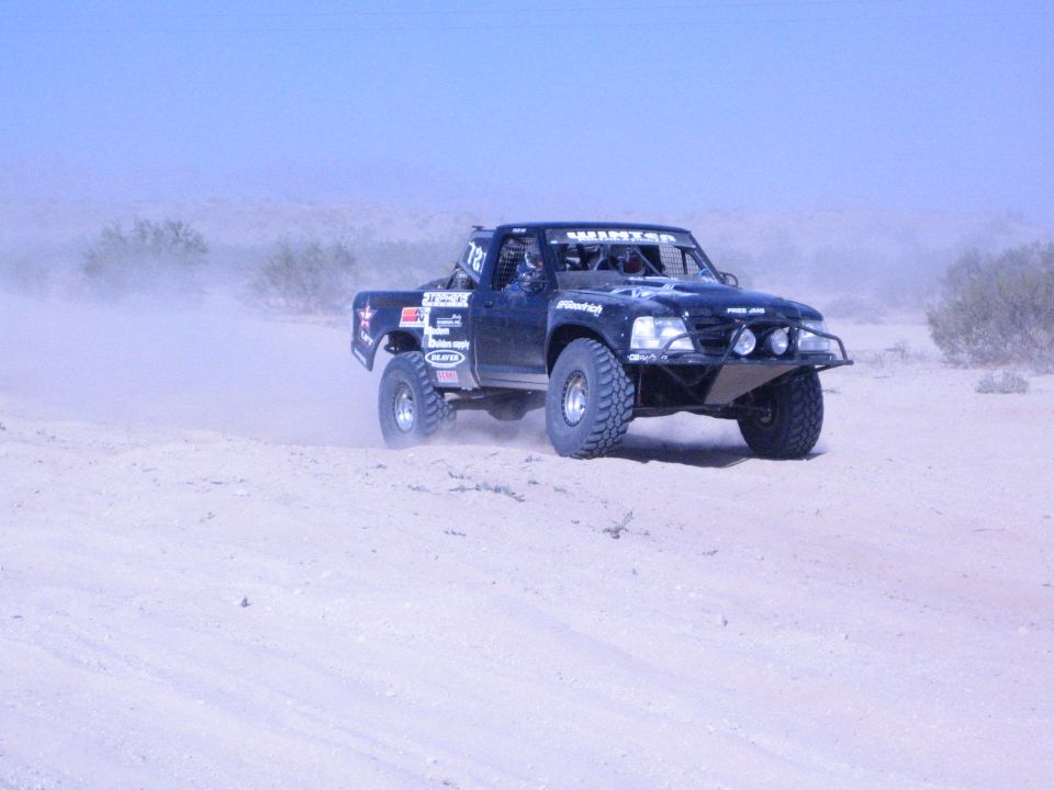 Black off-road race truck racing along a sandy desert track