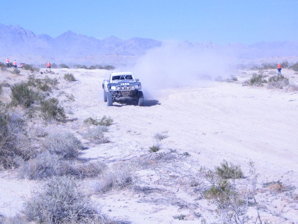 White off-road race truck kicking up dust on a sandy desert course