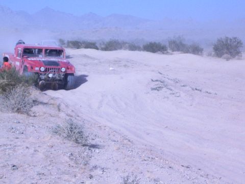 Red Hummer off-road race truck on a sandy desert ridge with mountains