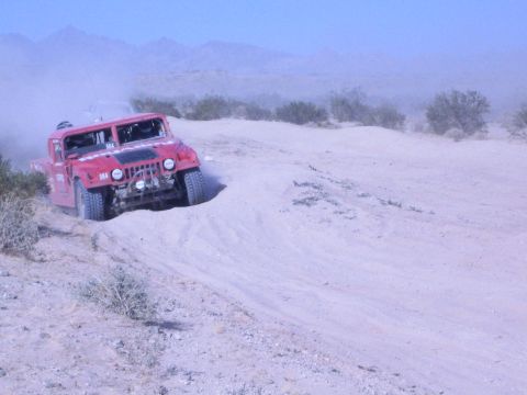 Red Hummer off-road race truck descending a sandy desert dune