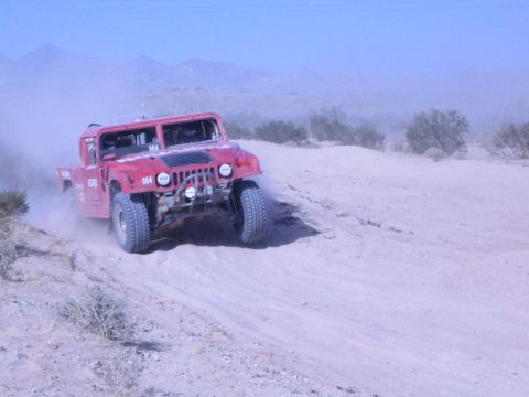 Front view of red Hummer off-road race truck climbing a sandy desert berm