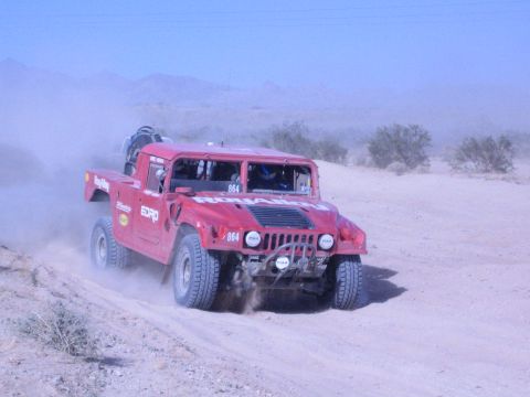 Red Hummer off-road race truck number 864 racing across desert sand