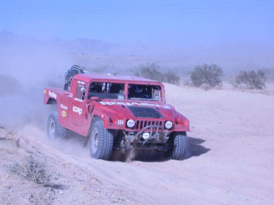 Red Hummer off-road race truck number 864 racing across desert sand