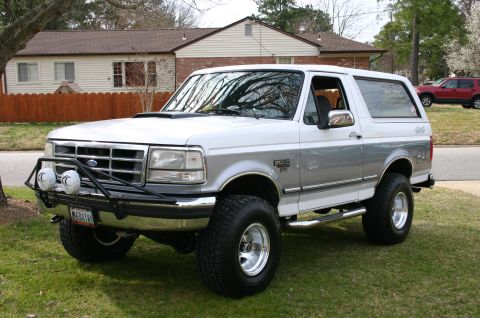 1994 Ford Bronco - A two-tone Ford Bronco is parked on a lawn in front of a house, with another vehicle visible in the background.