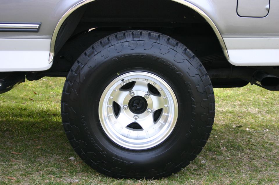 Front wheel and alloy rim with all-terrain tire on a lifted SUV over grass
