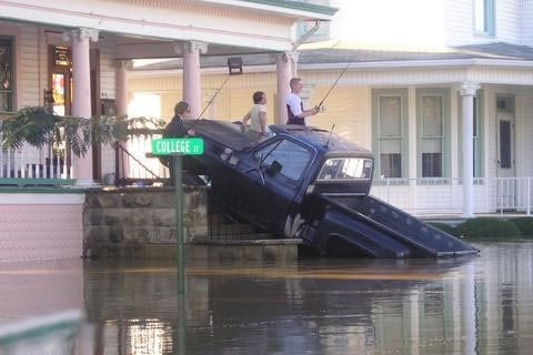 1966 Land Rover Discovery - A flooded street scene shows people fishing from the roof of a pickup truck, with a 'College' street sign nearby.
