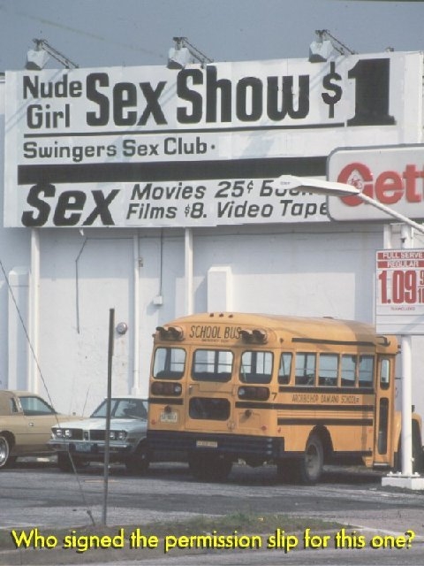 1966 Land Rover Discovery - A school bus and cars are parked in front of a large billboard advertising adult entertainment.
