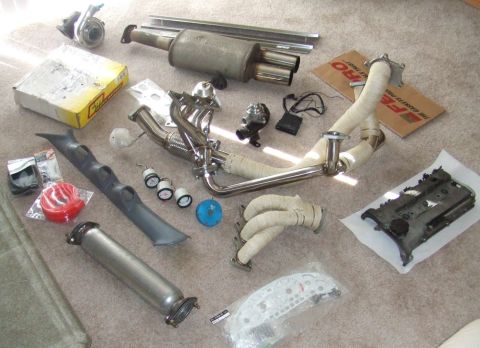 1995 Ford Probe - Various automotive performance parts are arranged on a carpeted surface, suggesting an upgrade or repair project.
