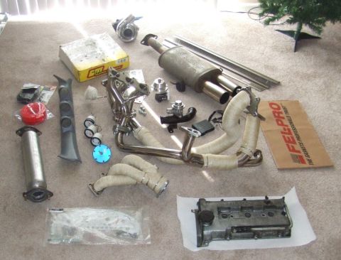1995 Ford Probe - Various automotive performance parts are laid out on the floor, including a turbocharger, exhaust system components, and gauges.
