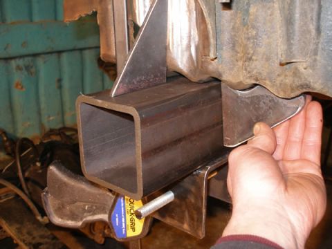 1994 Ford Bronco - Close-up of metal fabrication work on a vehicle frame, with a hand guiding a bracket into place.