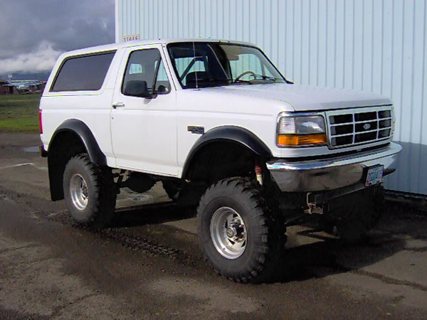 Lifted white Ford Bronco SUV with big off-road tires and black fender flares, 3/4 front view on wet pavement