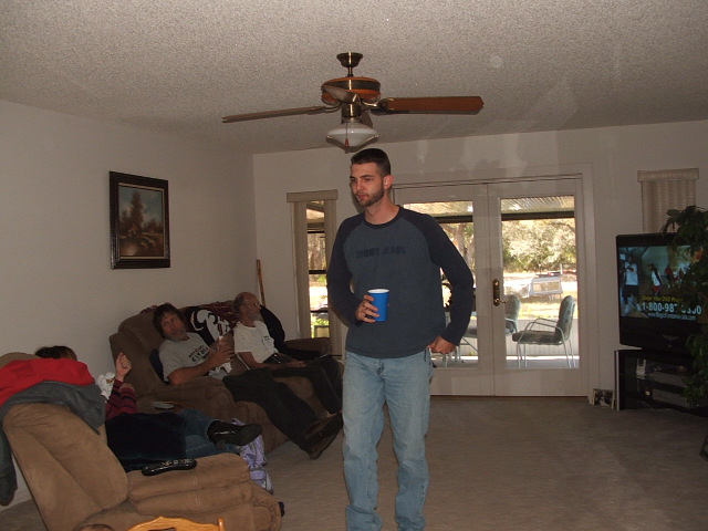 guy holding cup, people on couch, TV on, ceiling fan