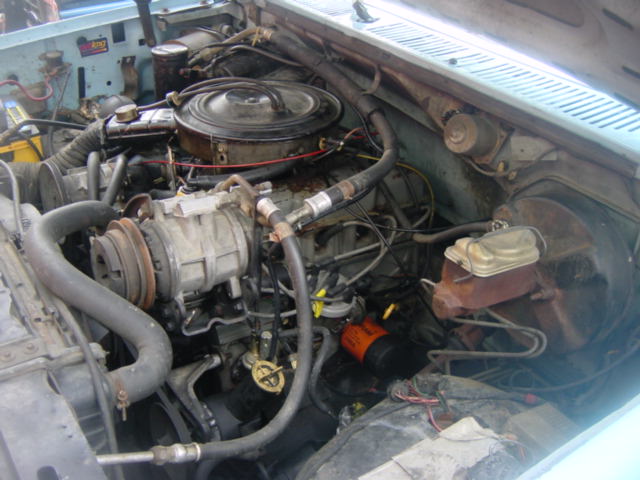 Engine bay with hoses, belts, and engine components visible. Some text on a yellow battery and an orange oil filter