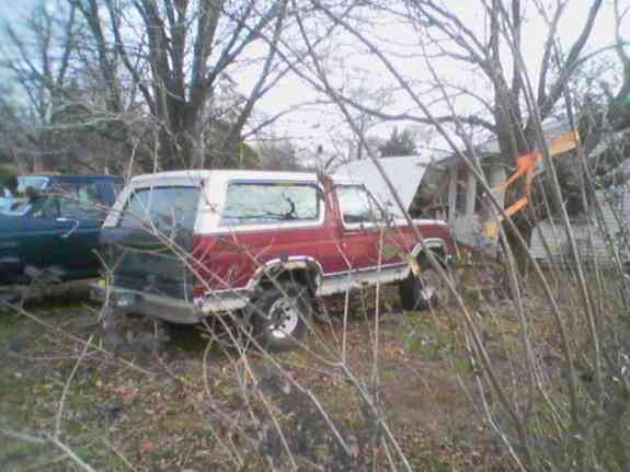 red and white SUV parked in overgrown yard, hood open, another dark SUV behind it