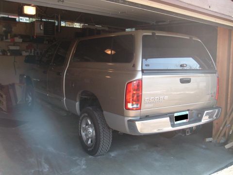 2004 Dodge 2500 - A tan Dodge Ram pickup truck with a cap is parked inside a garage.